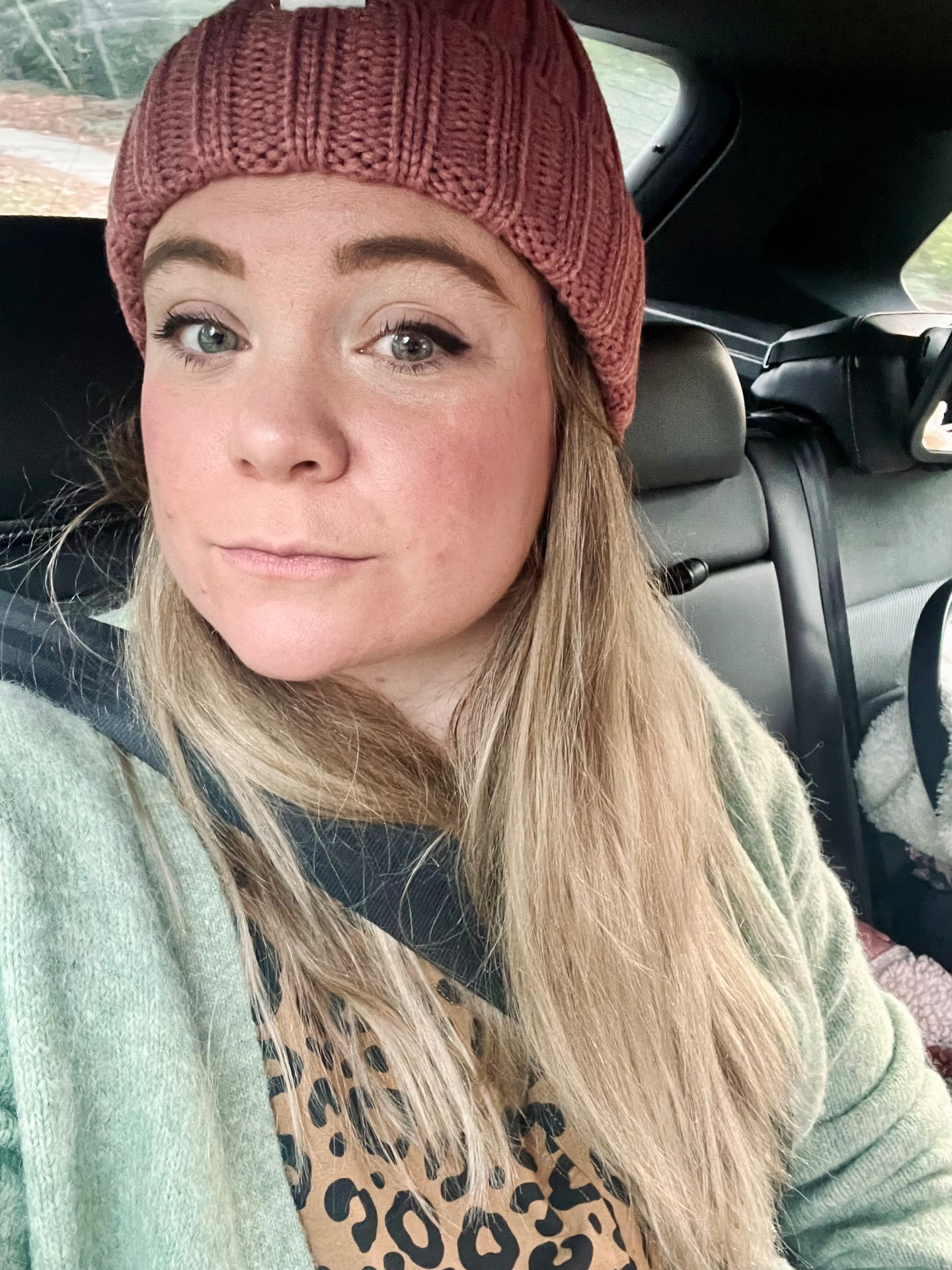 Rebecca, the founder of Family Prep, in a car wearing a pink beanie and sage green cardigan