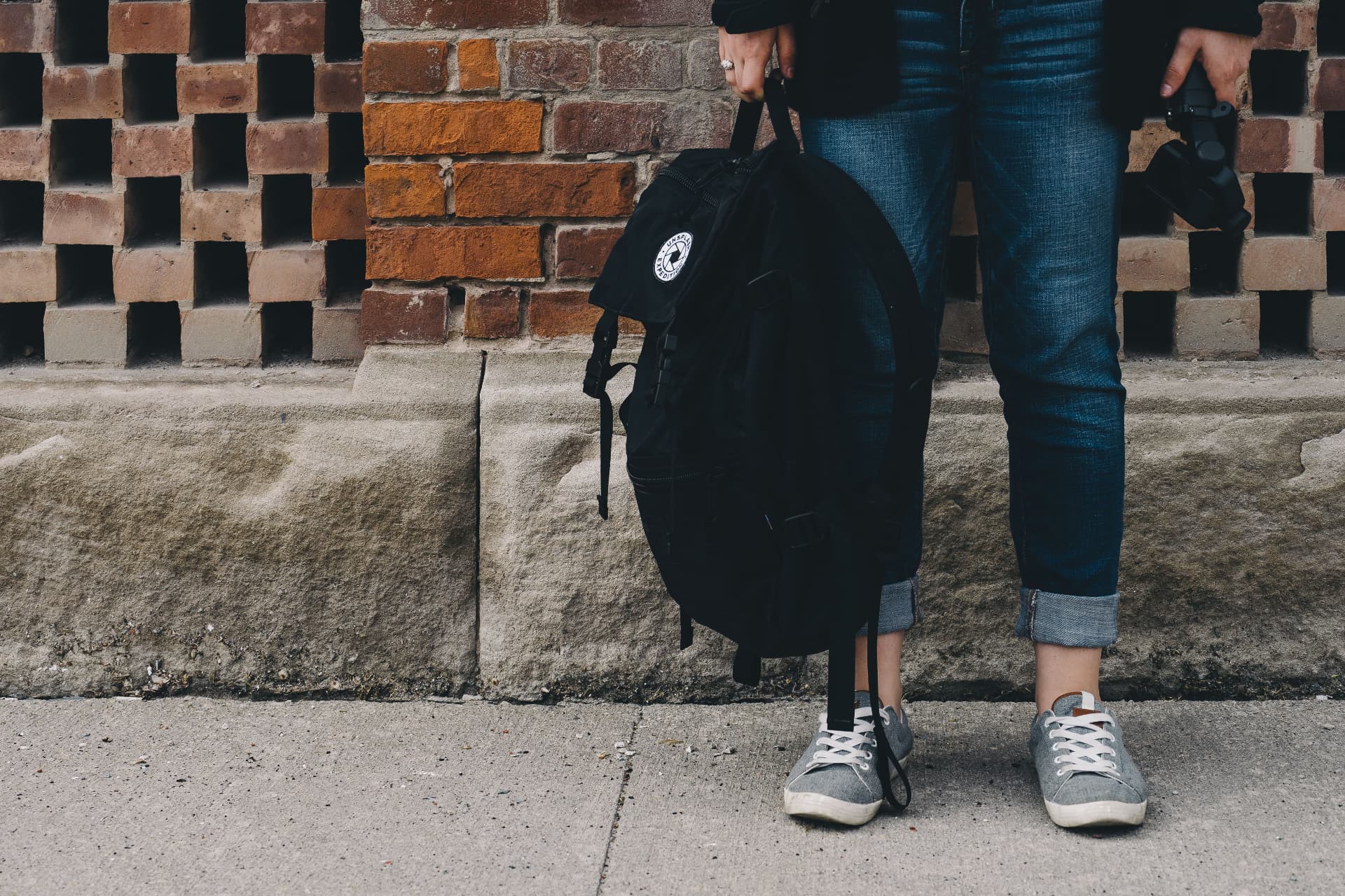A person holding a small black rucksack by the door