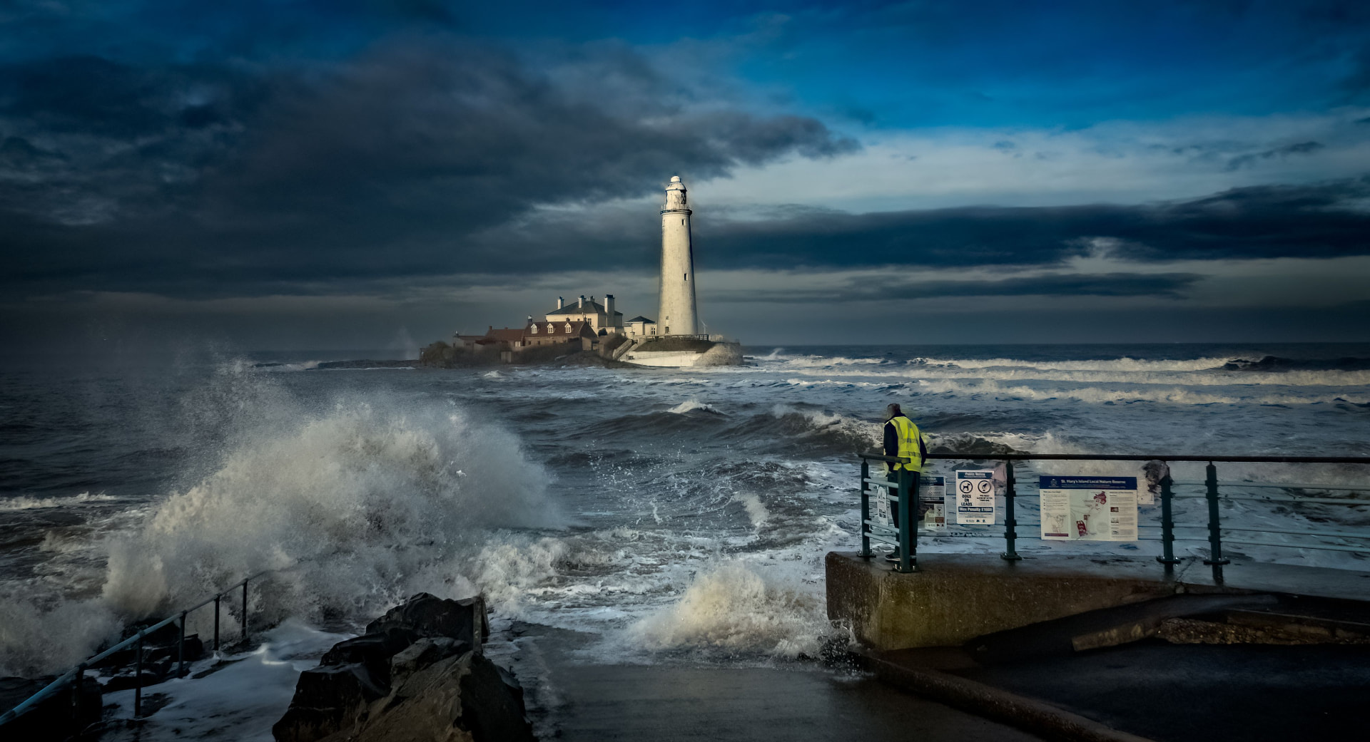 Waves crashing against the shore near a lighthouse under a dark, stormy sky