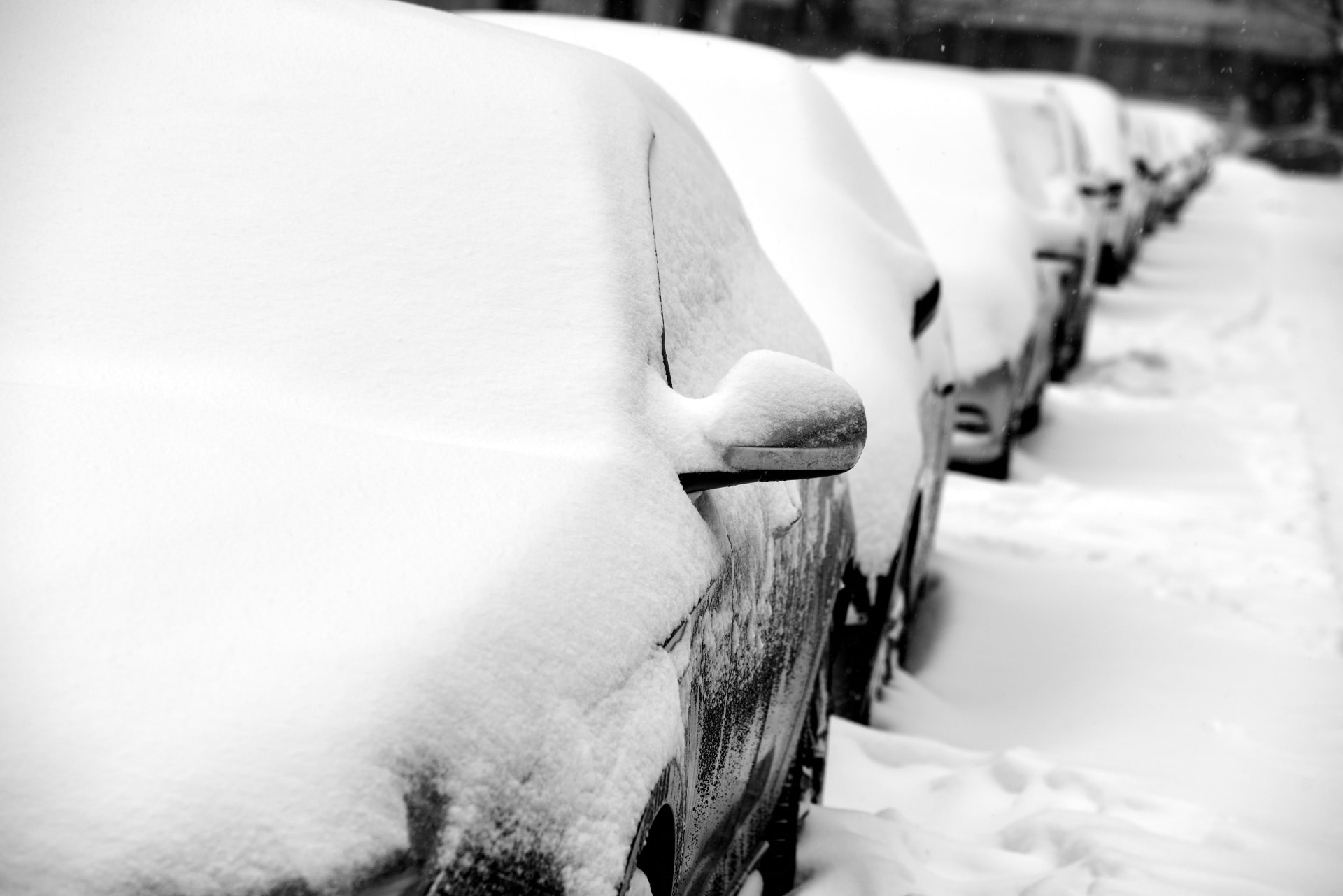 A row of parked cars covered in deep snow on a residential street